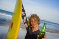 Young beautiful and happy surfer woman holding yellow surf board smiling cheerful drinking beer bottle enjoying summer holida Royalty Free Stock Photo