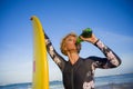 Young beautiful and happy surfer woman holding yellow surf board smiling cheerful drinking beer bottle enjoying summer holida Royalty Free Stock Photo
