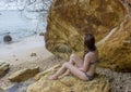 Young sexy beautiful pretty woman in bikini sitting on huge rock near ocean Royalty Free Stock Photo