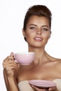 Young beautiful woman with dark hair picked up holding a ceramic cup and saucer pale pink drink tea or coffee on a white back