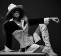 Young sexy beautiful woman in stylish costume, hat, fishnet tights and boots sitting and looking down over dark Royalty Free Stock Photo