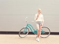 Young blond woman standing near a green vintage bicycle and holding a cup of coffeehave fun and good mood looking in camera a Royalty Free Stock Photo