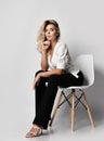 Keen attentive young blonde businesswoman in office pantsuit shirt and pants sits on chair leaning forward and looks at camera