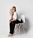 Young sexy blonde slim woman in office pantsuit shirt and pants sits on chair leaning forward and looks aside Royalty Free Stock Photo