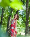 Young brunette girl in red dress posing on alley in summer park against trees Royalty Free Stock Photo