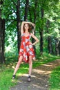 Young brunette girl in red dress posing on alley in summer park against trees Royalty Free Stock Photo