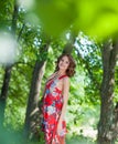 Young brunette girl in red dress posing on alley in summer park against trees Royalty Free Stock Photo