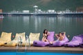 Young couple on cushioned loungers by swimming pool and lake on the background