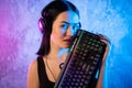 Young Disco Girl Wearing Gaming Headset Holding Gaming Keyboard. Room Lit in Retro, Retrowave or Cyberpunk Style