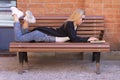 Young sexy girl with blond hair in sunglasses works on a laptop while lying on a bench