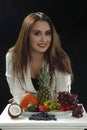 Young girl leaned on the stand and smiling close to assorti of differen fruits on black background