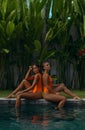 Young sexy girls in orange swimsuits posing in a pool at a tropical villa Royalty Free Stock Photo
