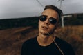 Young sexy man in black shirt and sunglasses standing outdoor. Dark key photo