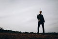 Young sexy man in leather jacket and sunglasses standing outdoor. Dark silhouette against grey sky