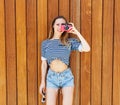 Young smiling photographer woman, holding and making picture on retro pink vintage camera, wearing bright marine clothes, joy