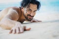 Young sexy stylish handsome latin man lies on tropical beach with sand on skin, sunbathing vacation concept