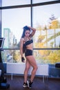 Young woman with beautiful body and long dark hairs posing near panoramic window in fitness club. City, autumn yellow trees a Royalty Free Stock Photo