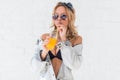 Young woman drinking orange juice or cocktail wearing sunglasses bra and jeans jacket Outdoors, lifestyle. Royalty Free Stock Photo