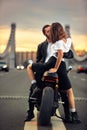 Young sexy woman hugging cute man in stylish black leather jacket, sitting on sports motorcycle on the bridge in the Royalty Free Stock Photo