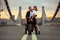 Young sexy woman hugging cute man in stylish black leather jacket, sitting on sports motorcycle on the bridge in the Royalty Free Stock Photo