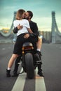 Young sexy woman hugging cute man in stylish black leather jacket, sitting on sports motorcycle on the bridge in the Royalty Free Stock Photo