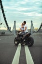 Young sexy woman hugging cute man in stylish black leather jacket, sitting on sports motorcycle on the bridge in the Royalty Free Stock Photo