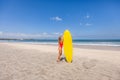 Young sexy woman in red swimwear holding a surfboard alone on the Bali beach Royalty Free Stock Photo