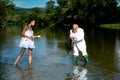 Young sexy woman and old fisherman standing in river with fishing rod. Father and daughter fishing. Mature man fisher