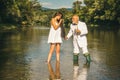 Young sexy woman and old fisherman standing in river with fishing rod. Old senior and girl fishing.