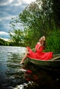 Young sexy woman in red dress on boat. The girl has a flower wreath on her head, relaxing and seiling on river Royalty Free Stock Photo