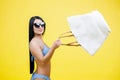 Young sexy woman slim body wearing in blue swimsuit and with sunglasses holding big shopper bag, walking on isolated on yellow Royalty Free Stock Photo