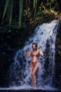 Young and woman with a sporty body posing in a swimsuit near the beautiful waterfall Royalty Free Stock Photo