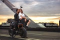 Young sexy woman hugging cute man in stylish black leather jacket, sitting on sports motorcycle on the bridge in the Royalty Free Stock Photo