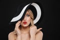 Young shocked blonde woman with bright makeup red lips posing isolated over black wall background wearing hat Royalty Free Stock Photo
