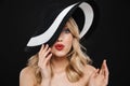 Young shocked blonde woman with bright makeup red lips posing isolated over black wall background wearing hat Royalty Free Stock Photo