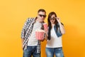 Young shocked couple woman and man in 3d glasses watching movie film on date holding bucket of popcorn drinking soda or Royalty Free Stock Photo