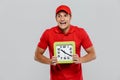 Young shocked delivery man in uniform screaming while showing clock