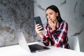 Young shocked woman sitting indoors laptop computer chatting by mobile phone Royalty Free Stock Photo