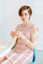 Young short-haired woman crochet handmade dress for her hobby sitting in kitchen in sunny morning. Business crochet handmade home