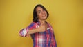 Young short-haired woman with dark hair on yellow background stands and demos her finger up. Model shows thumb up.
