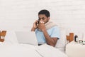 Young sick black man working on laptop in bed