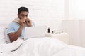 Young sick black man working on laptop in bed