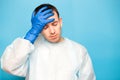 Young sick doctor man touching his head with hand in gloves isolated on blue Royalty Free Stock Photo