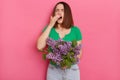 Young sick girl with brown hair holding bouquet of lilac flowers, sneezing, keeps eyes closed, reacts on trigger suffers fro