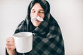 Young sick man isolated over white background. Guy covered with blanket. Holding cup of tea with closec nose tissues Royalty Free Stock Photo