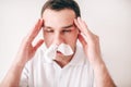Young sick man isolated over white background. Portrait of guy with tissues in nose holding hands on headache. Guy Royalty Free Stock Photo