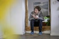 Young sick man with a scarf, sitting yawning in a door frame holding a thermometer and a cup of tea in his hands Royalty Free Stock Photo