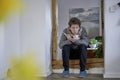 Young sick man with thermometer, blowing into his tea while sitting in a door frame, wearing a scarf Royalty Free Stock Photo