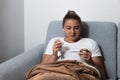 Young sick stressed woman lying at home covered with blanket checking her body temperature. Ill female have common cold and flue m Royalty Free Stock Photo