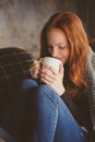 Young sick woman healing with hot drink at home on cozy couch